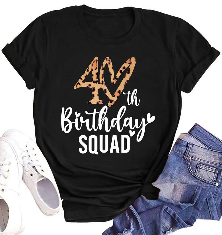 A black short-sleeve T-shirt laid flat with a leopard-print '40th Birthday SQUAD' graphic on the front, styled with white sneakers and blue denim shorts on a white background.