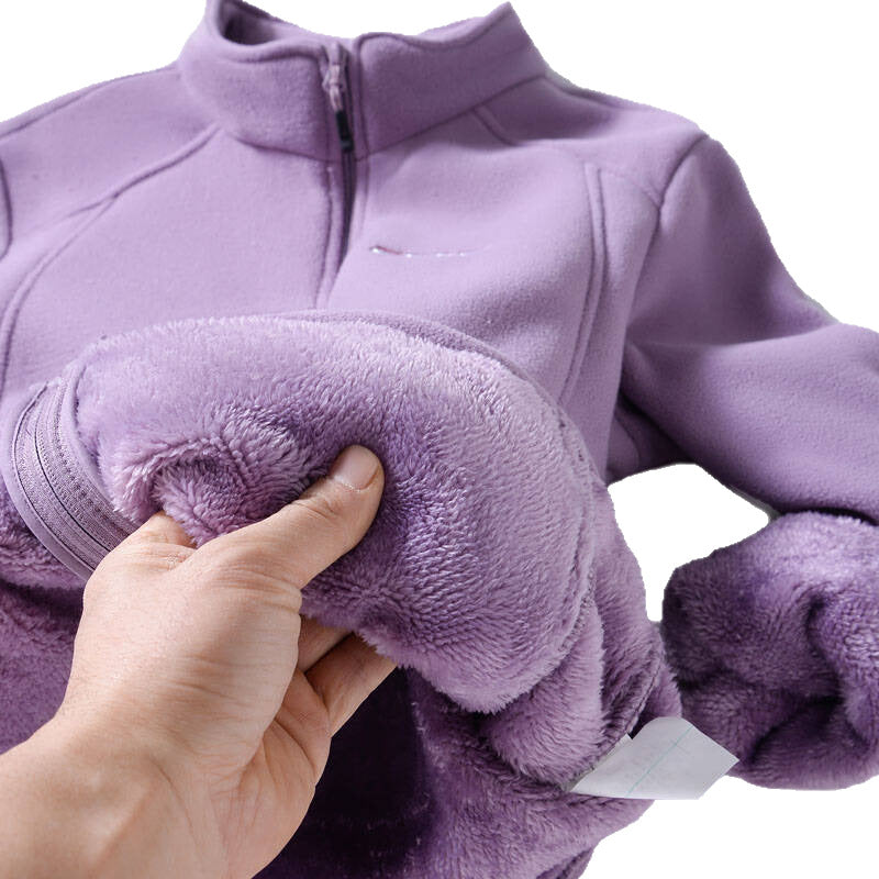 A close-up of a purple fleece zip-up jacket being held open by a hand to show the soft, plush lining. The jacket has a mock neck collar and a partial zipper, with the thick textured fabric lining pulled outwards.