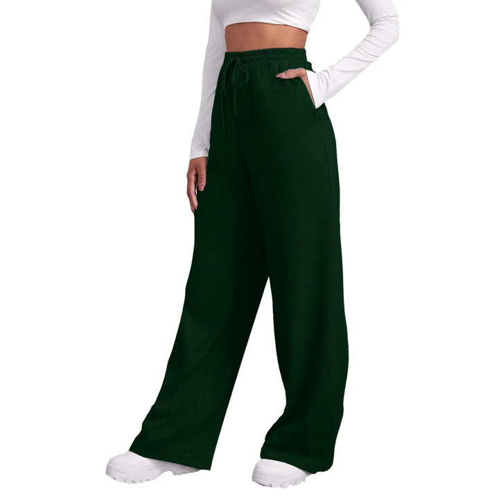 A person wearing dark forest green wide-leg drawstring pants with side pockets, styled with a white long-sleeve crop top and white sneakers against a plain white background.