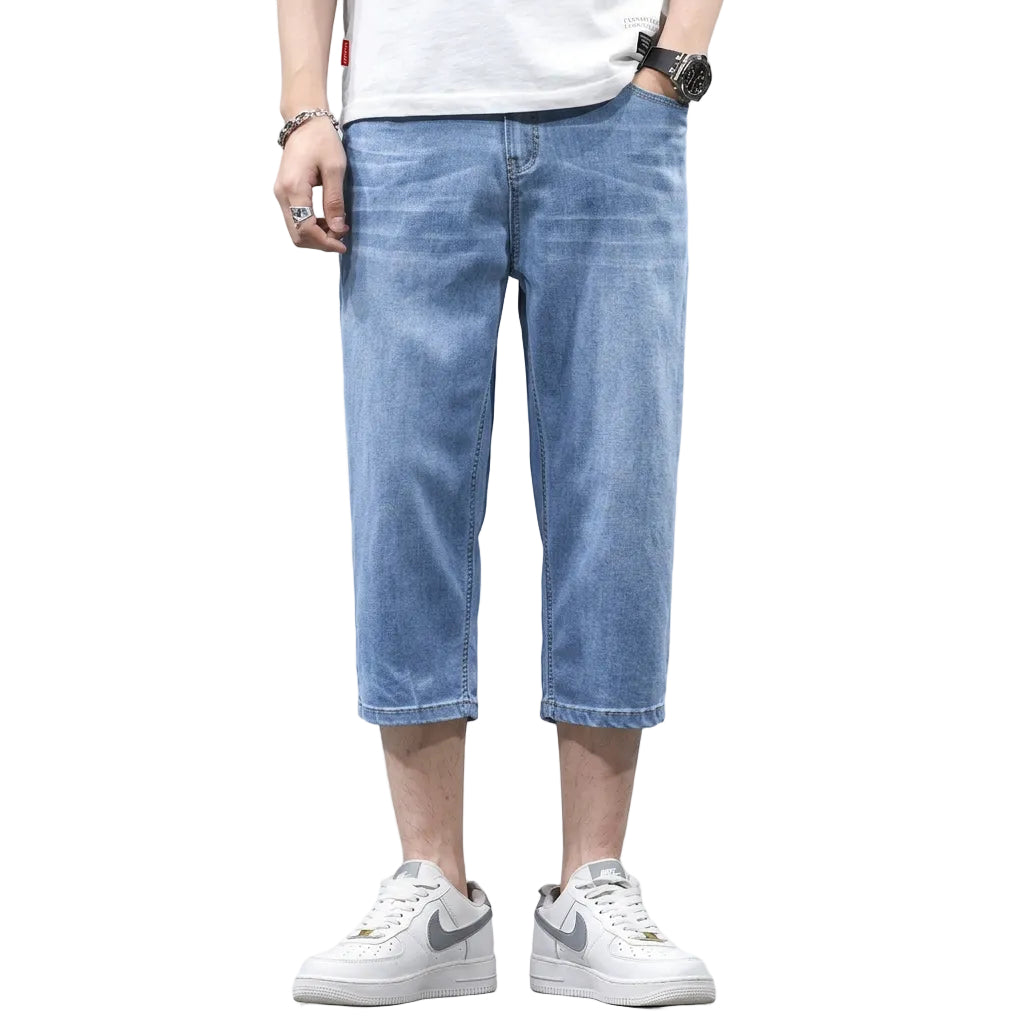 A person modeling light blue cropped denim shorts with a white t-shirt and white sneakers, standing against a dark gray wall with promotional text that reads 'Look taller and slimmer' and small inset views showing the shorts from the back and front.