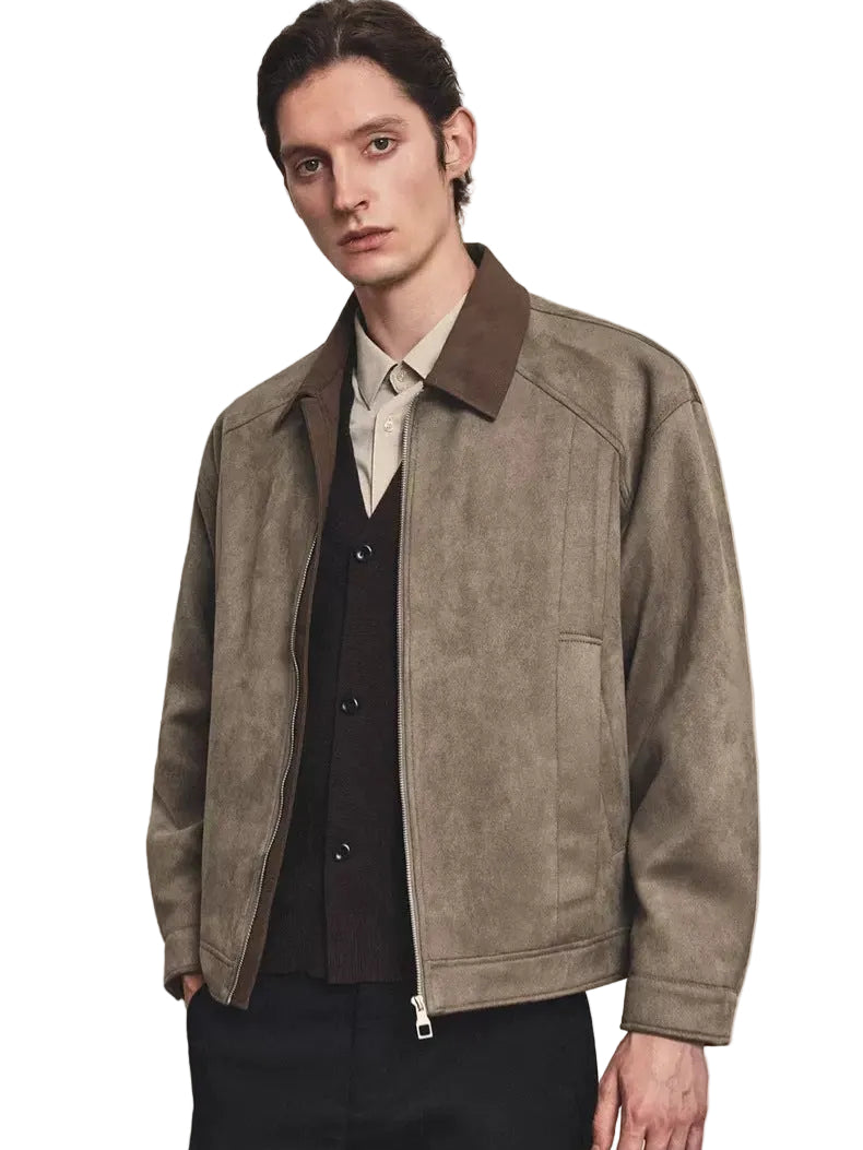 A man wearing a taupe-brown suede jacket with a contrasting dark brown collar, layered over a dark vest, cream shirt, and black trousers, set against a textured light gray background.