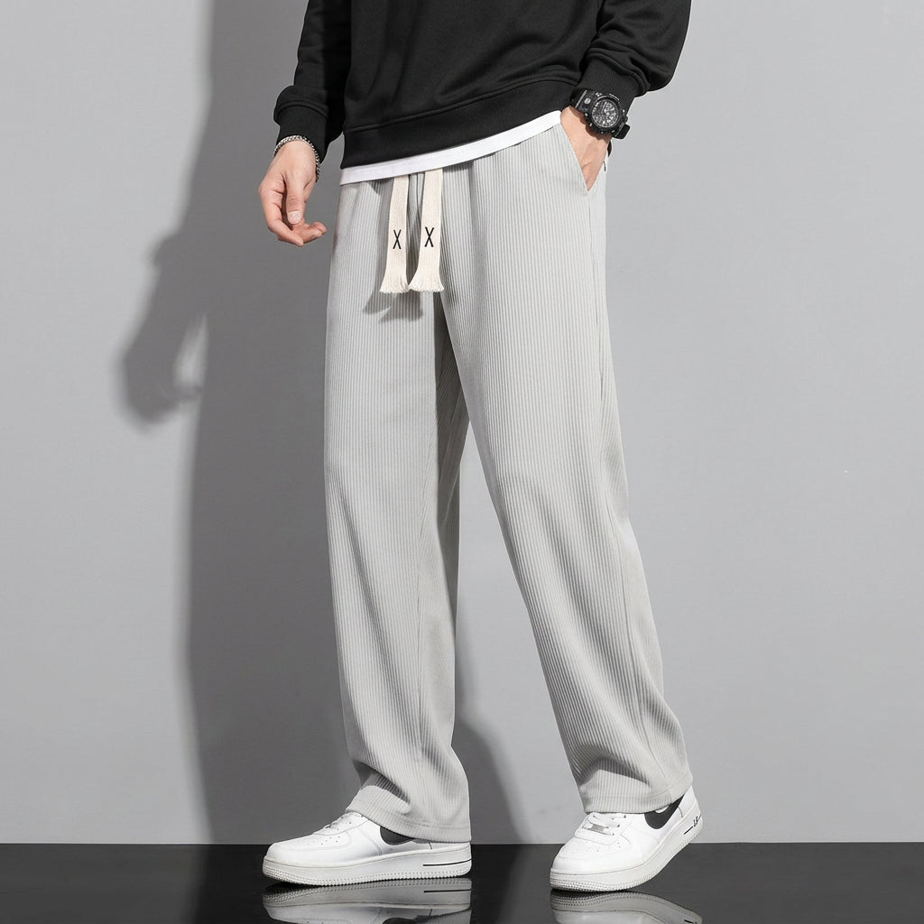 Person wearing light gray pants with a black top and white sneakers on a gray background