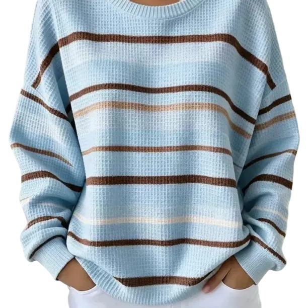 A person wearing a light blue waffle-knit sweater with horizontal brown and beige stripes, standing outdoors with hands in the pockets of white pants.