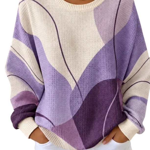 A person wearing a waffle-knit sweater with a large abstract wavy pattern in cream, light purple, and dark purple, paired with white pants.