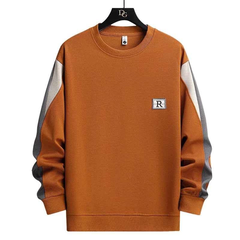 A men's crewneck sweatshirt in a warm rust-orange color, featuring color-blocked light gray sleeves and a small square chest patch with the letter 'R'. The sweatshirt is displayed on a black hanger against a solid white background.