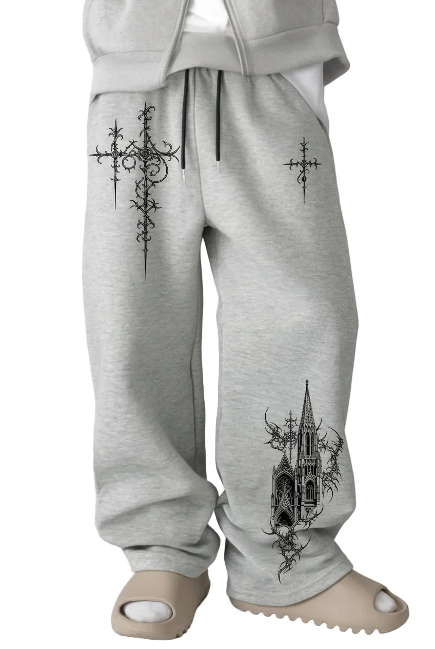 Light gray sweatpants with black gothic-style cross and cathedral graphic prints, shown on a person seated in front of a dark couch.