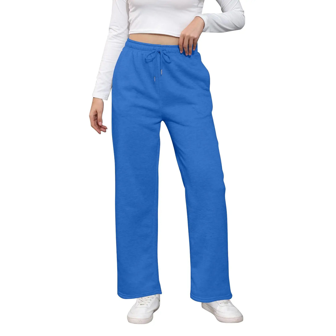 A person wearing bright blue drawstring sweatpants with a white long-sleeve crop top and white sneakers, shown against a plain white studio background.