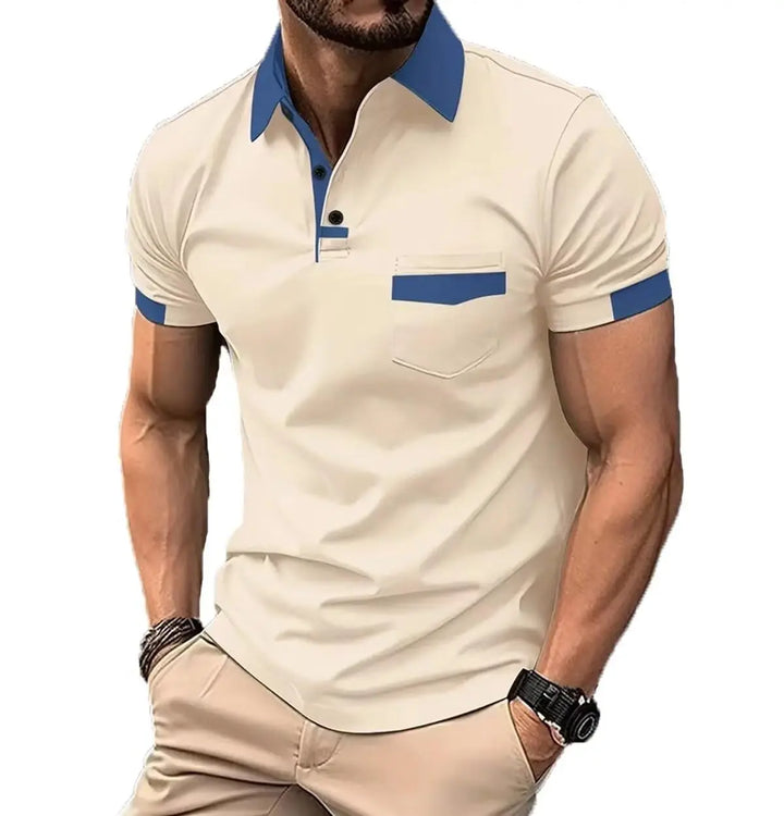 A man wearing a beige short-sleeve polo shirt with a contrasting blue collar, button placket, and sleeve cuffs, paired with beige trousers against a plain white background.