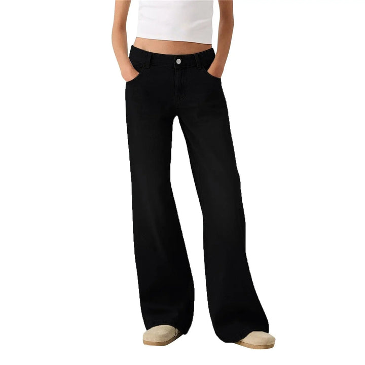 A person wearing loose black wide-leg jeans with a white cropped top and beige slip-on shoes, shown from the waist down against a plain white background.