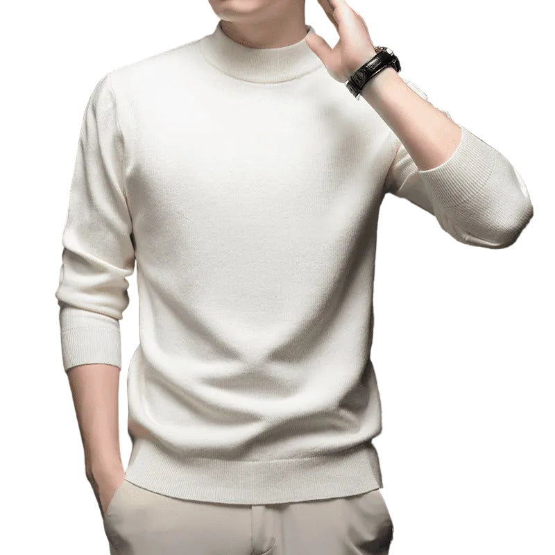 A man wearing a cream-colored, long-sleeve mock neck knit sweater and matching trousers, shown from the chin down against a dark studio background.