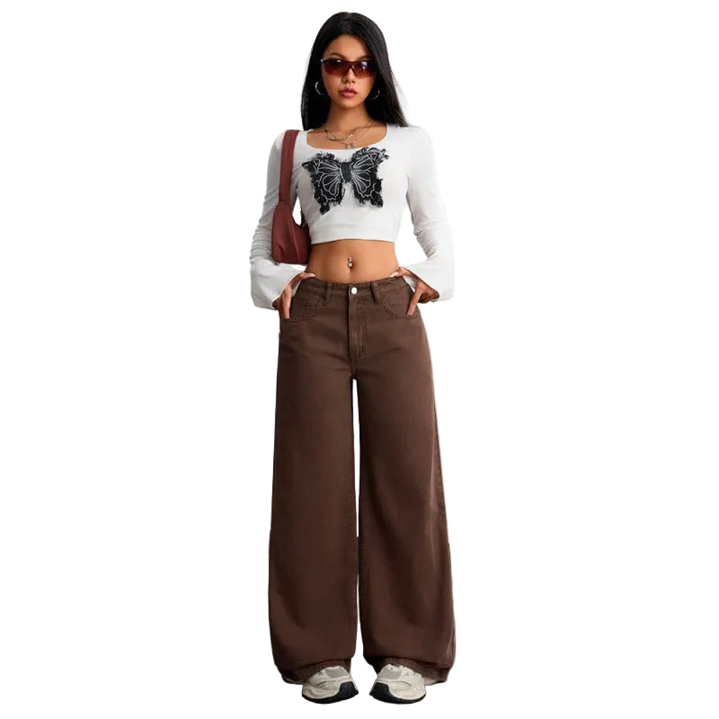 Woman wearing a white long-sleeve crop top with a butterfly design and brown wide-leg pants, standing against a plain background.