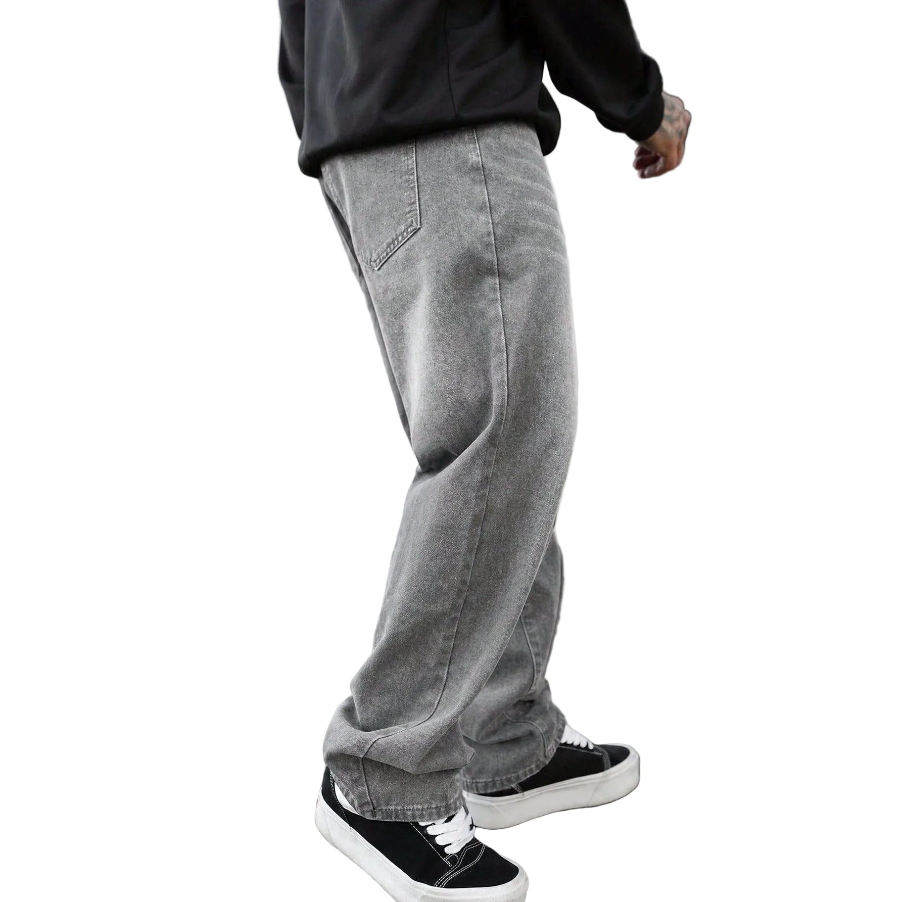 A person wearing loose-fit gray washed denim jeans, a black hoodie, and black low-top sneakers with white soles, standing on a paved sidewalk in front of a modern building.