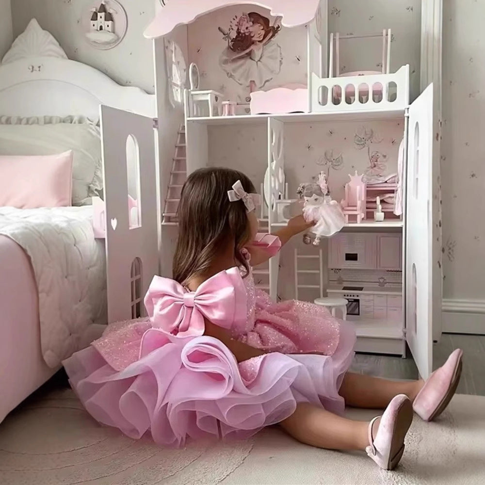 Young girl in a pink dress playing with dolls in a dollhouse-themed room.