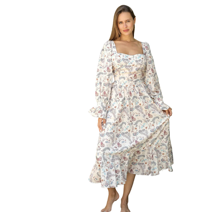 Woman in a floral dress standing outdoors with greenery and a white fence in the background.