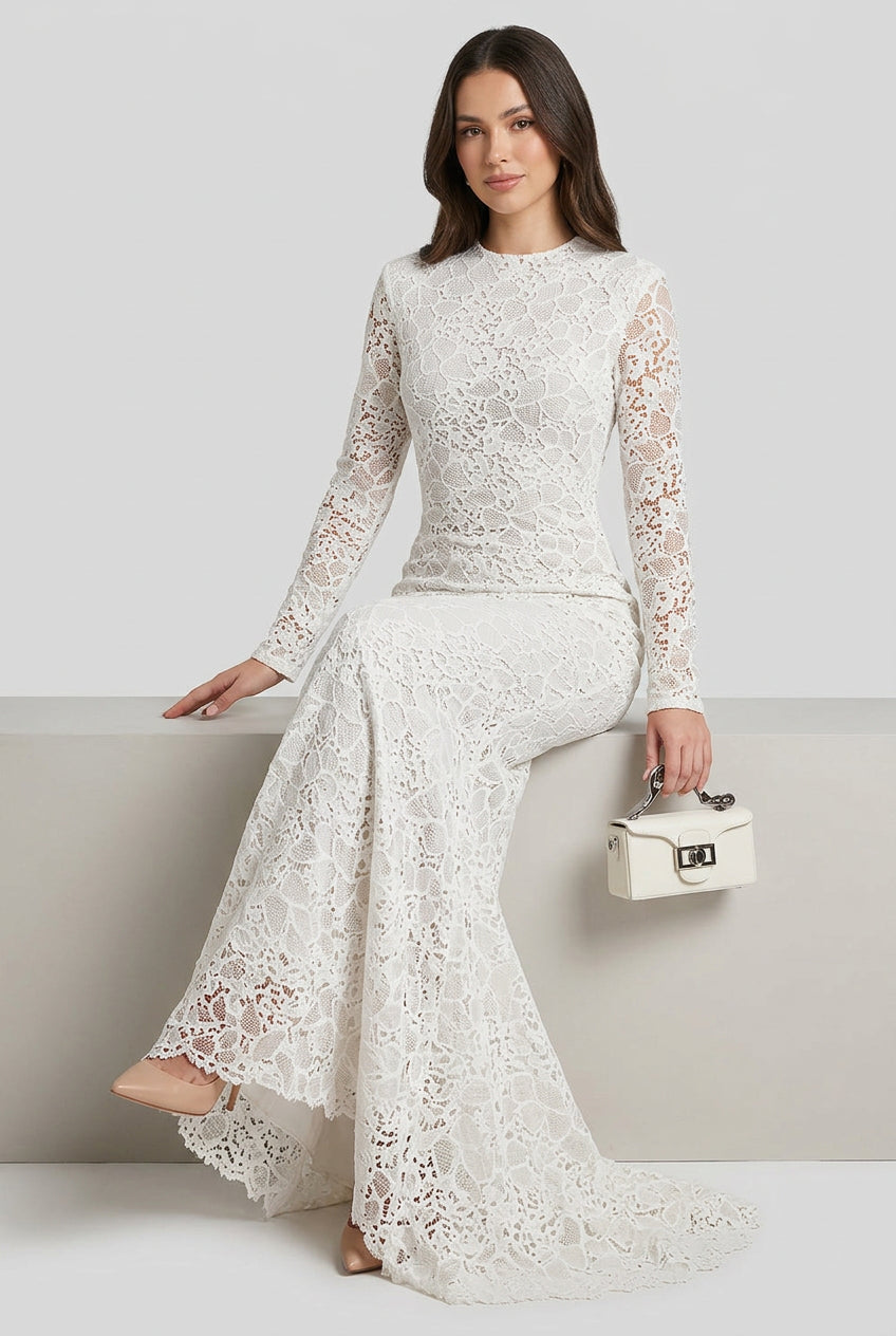 A woman wearing a fitted long-sleeve lace dress sits on a red patterned staircase, holding a small cream handbag.