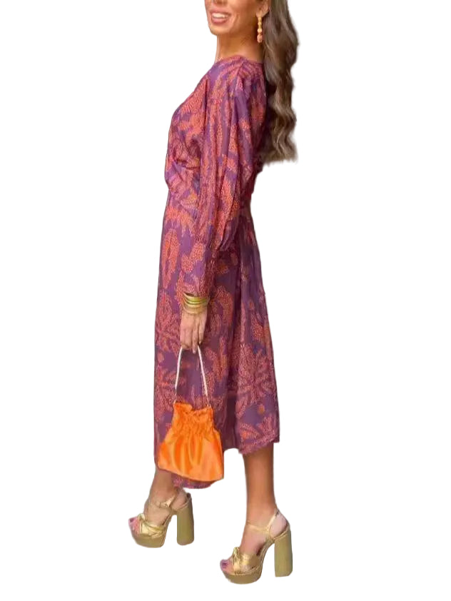 Woman in a patterned dress holding an orange bag against a black wall.