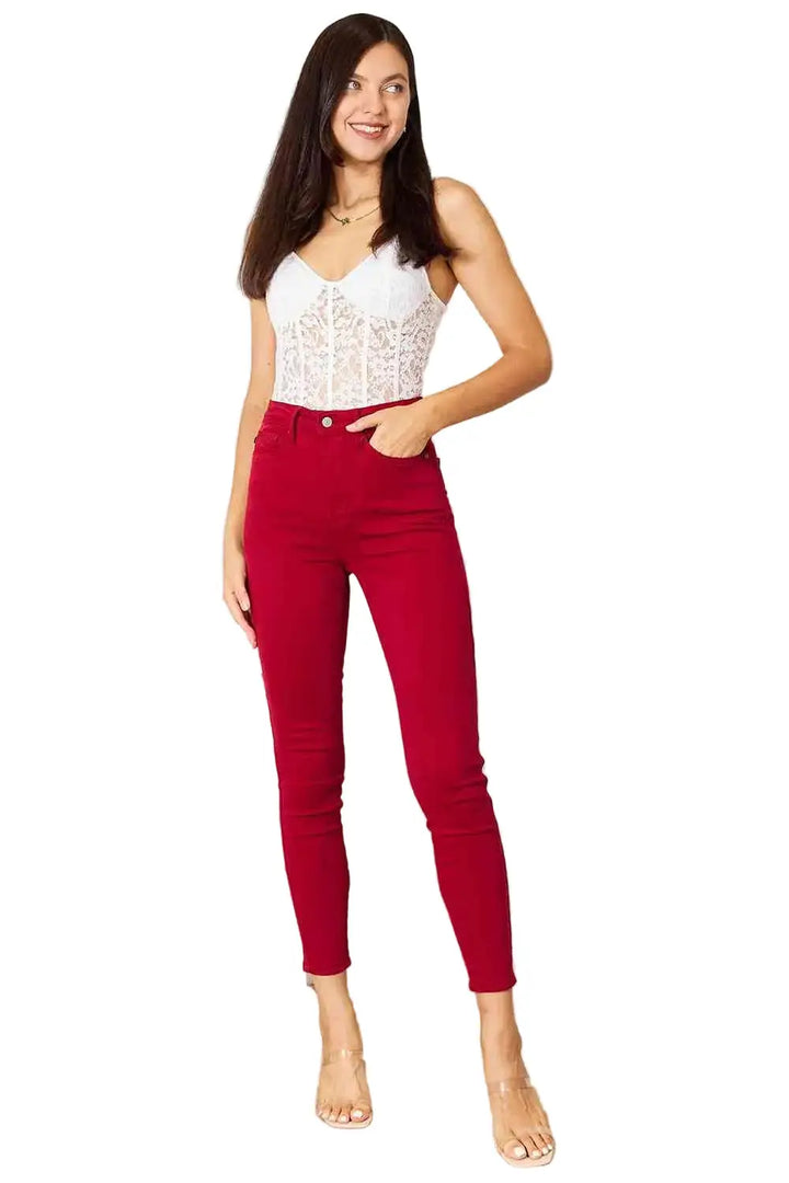 Woman wearing red pants and a white top in a room with a white dresser and curtains.