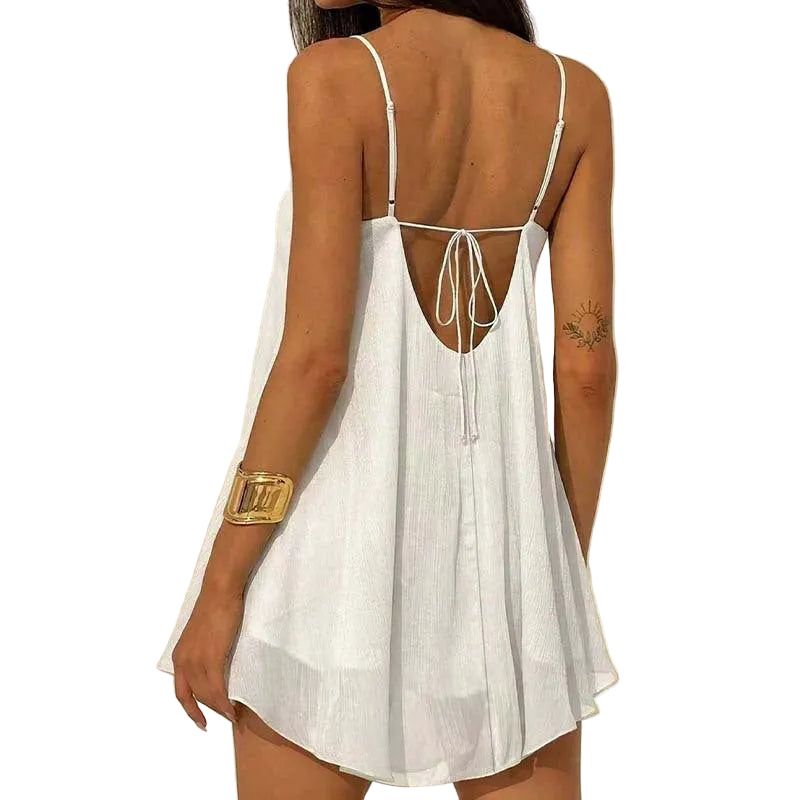 A woman shown from the back wearing a white sleeveless mini dress with thin straps and a tie-back neckline, photographed against a plain light beige wall.