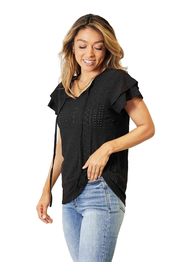 Woman wearing a black top with ruffled sleeves and blue jeans in a bright room.