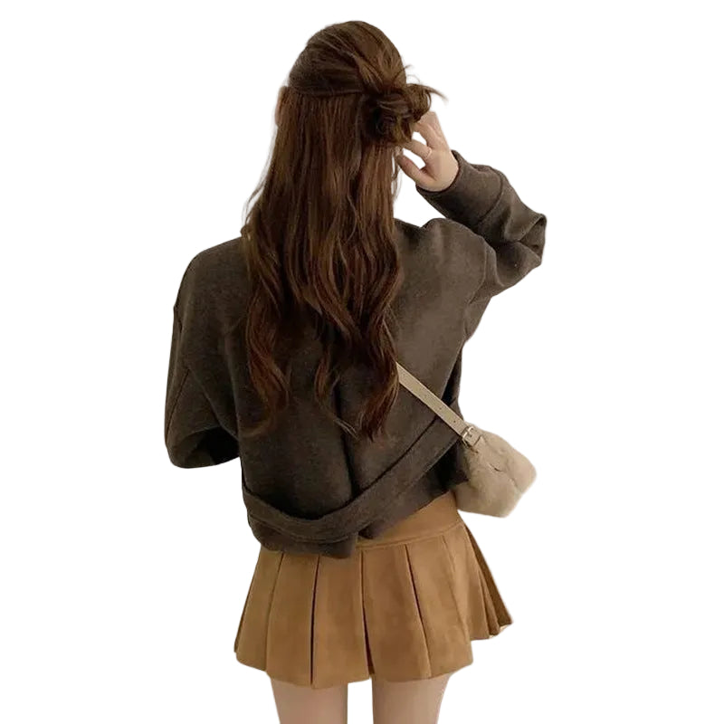 A woman shown from behind wearing a dark brown cropped knit sweater, a tan pleated skirt, and carrying a small tan shoulder bag against a plain white background.