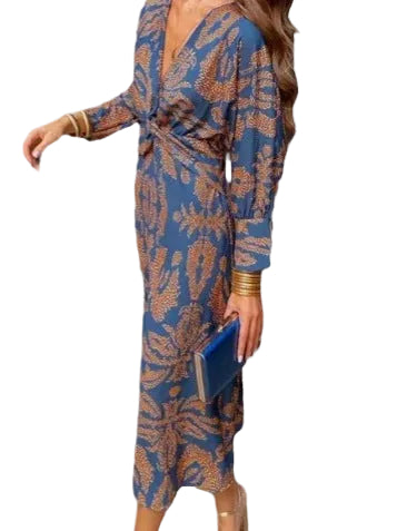A woman wearing a long-sleeve wrap-style midi dress with a blue base and brown floral pattern, holding a blue clutch against a plain white background.