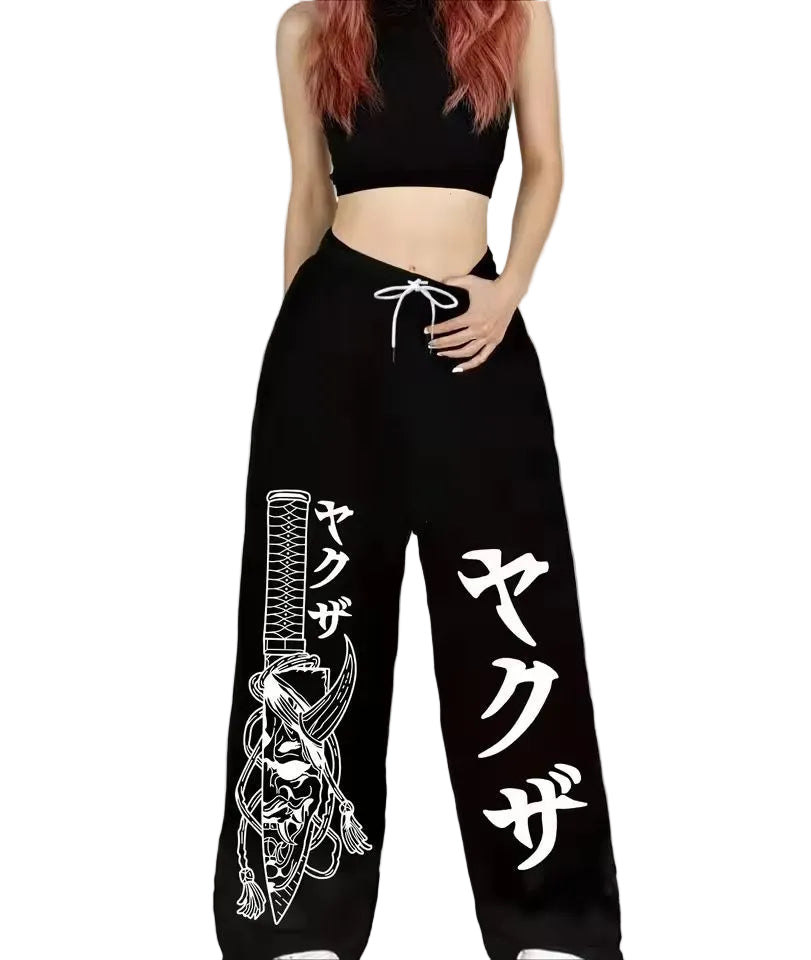 A model wearing black wide-leg sweatpants with white Japanese text and a white sword graphic, paired with a black crop top against a light gray background.