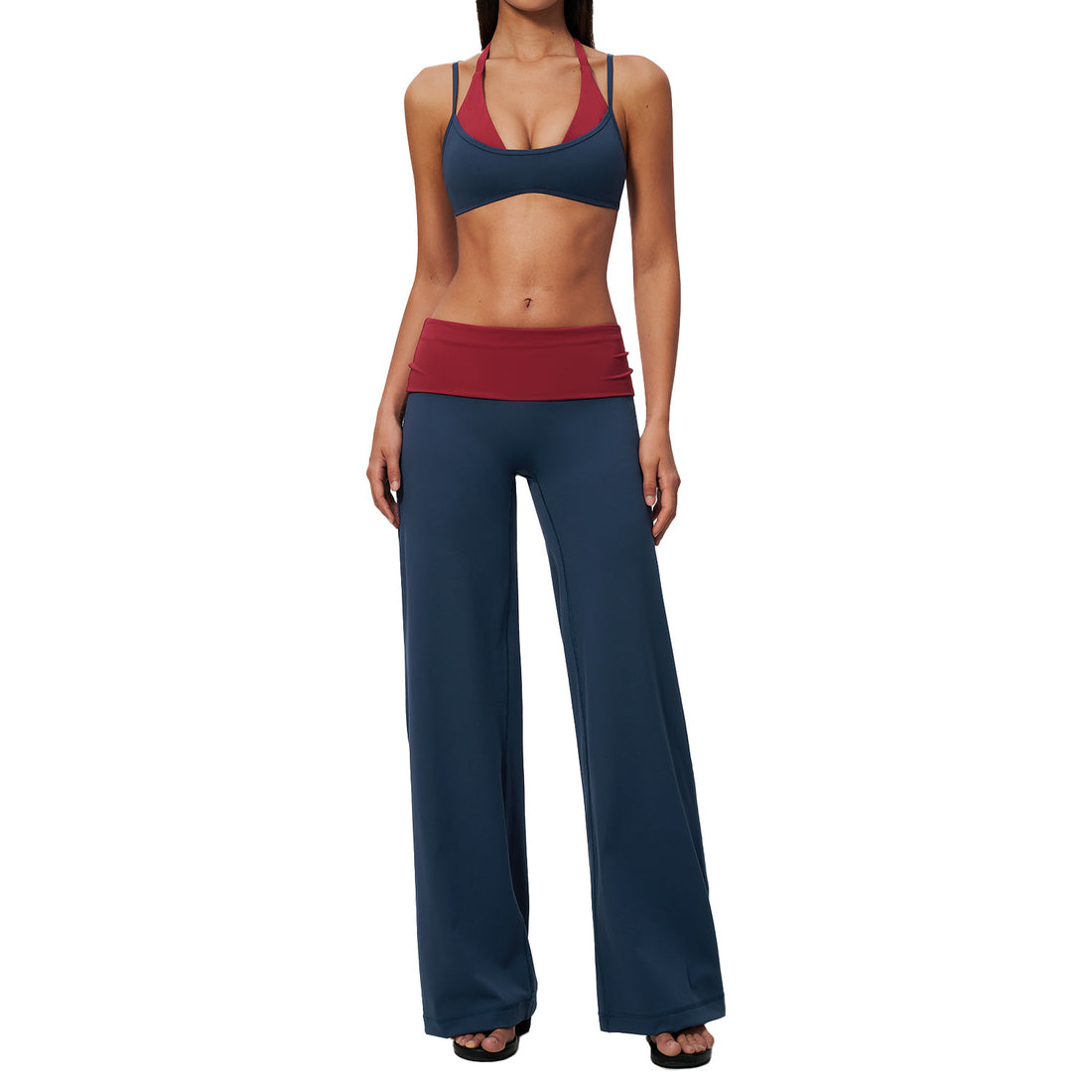 A woman modeling a two-piece activewear set consisting of wide-leg navy blue pants and a matching navy sports bra with a contrasting red underband, set against a plain white background.