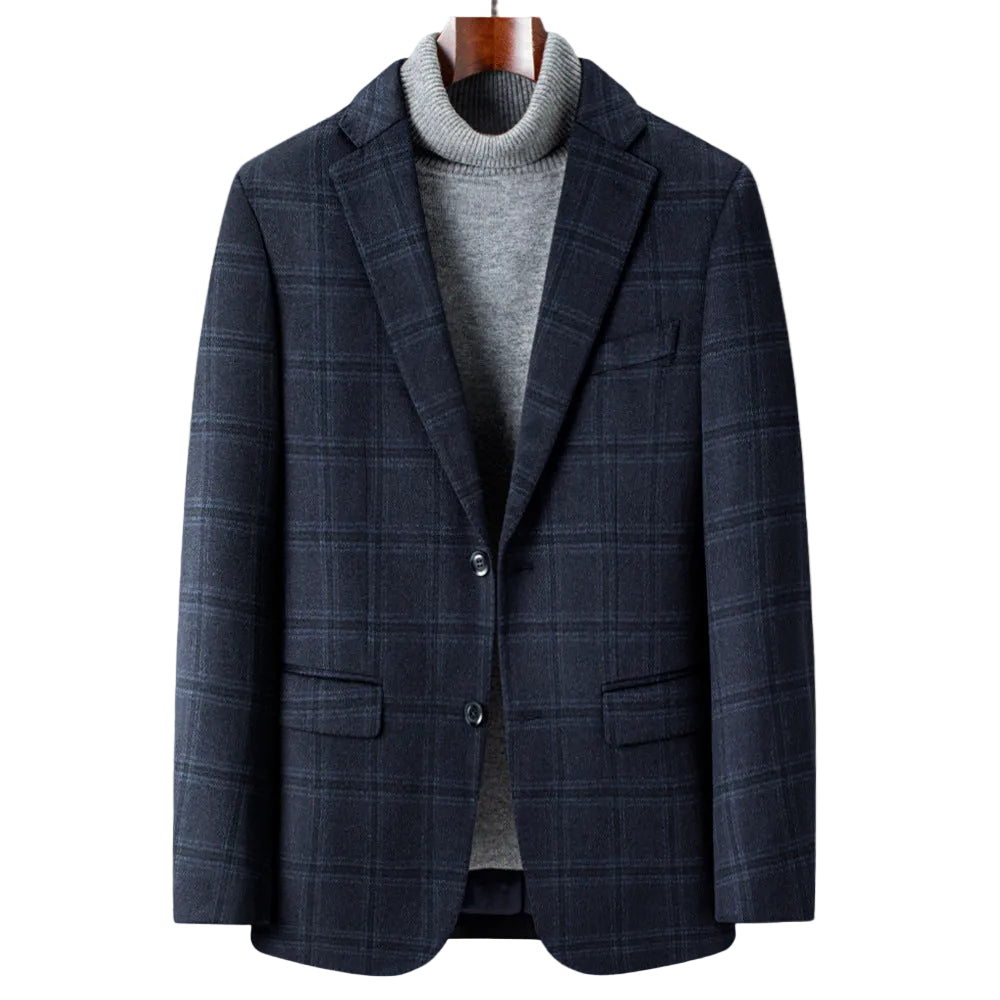 A men's navy blue plaid blazer styled over a gray turtleneck sweater, displayed on a wooden hanger against a warm beige background with a white vase on a wooden table.