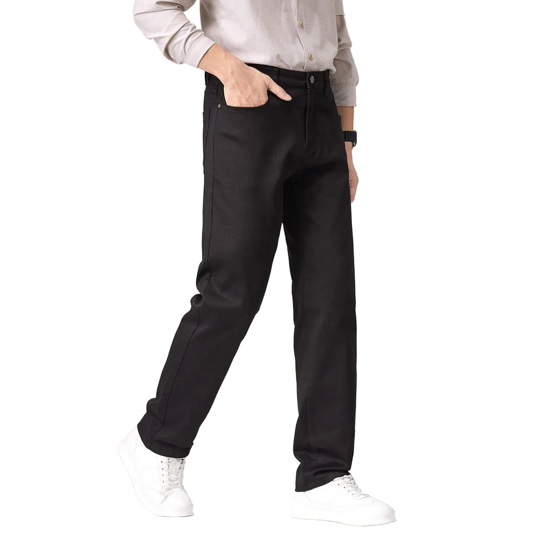 A person wearing black straight-leg jeans with a light beige button-up shirt and white sneakers, standing against a plain light gray studio background.