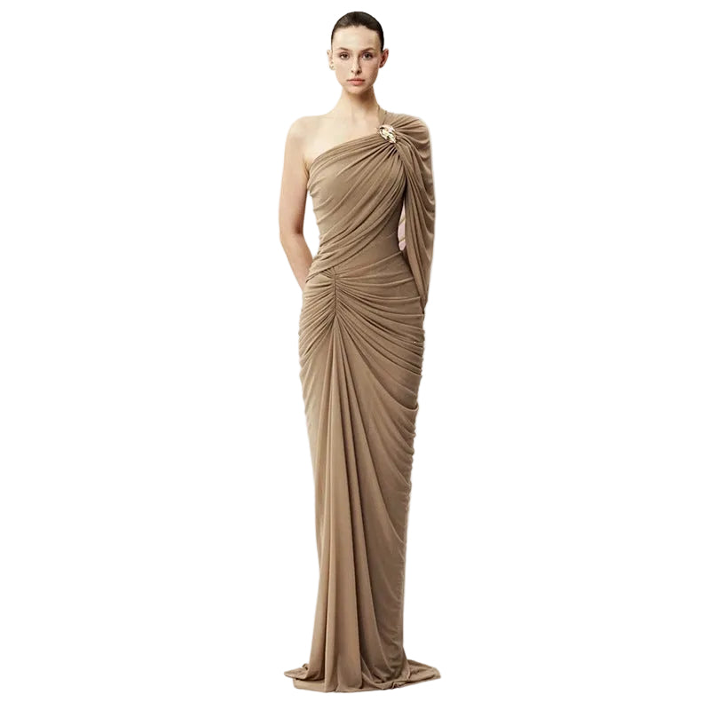 A woman modeling a floor-length draped gown in a warm taupe-brown shade against a plain white studio background.