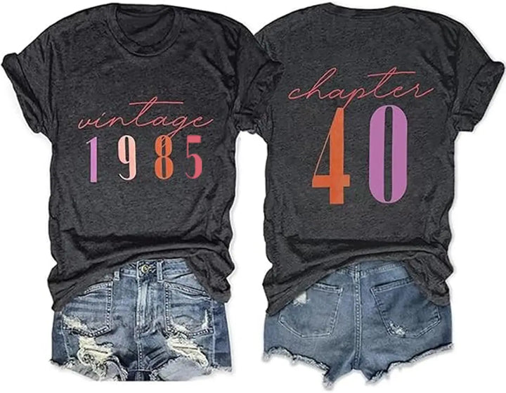 Two black graphic T-shirts shown front and back, styled with distressed denim shorts on a white background. The front reads 'vintage 1985' in pink, orange, and purple.