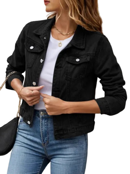 Person wearing a black denim jacket, white shirt, and blue jeans against a beige wall.