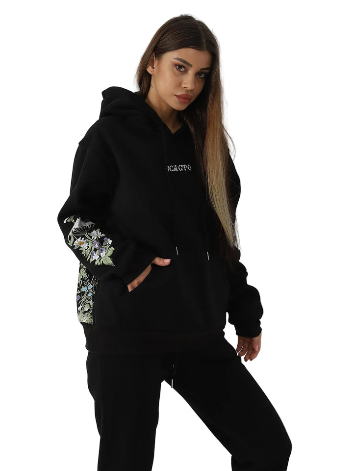 Woman wearing a black hoodie with floral sleeves against a white wall