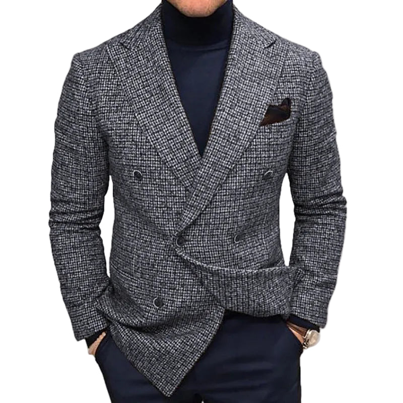 A man wearing a double-breasted blazer in a gray and black micro-check pattern over a dark navy turtleneck sweater and navy trousers, shown from the chin down against a light gray studio background.