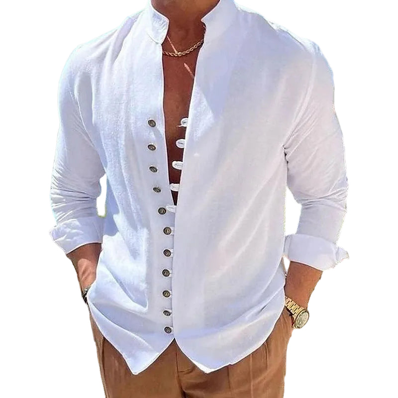 A man wearing a white long-sleeve button-front shirt with a mandarin collar, styled with tan pants in an outdoor setting with wicker furniture and a beach background.