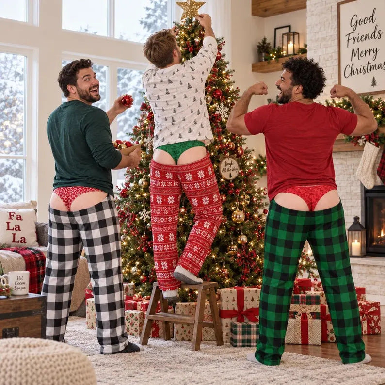 Three men in a cozy living room setting, wearing matching Christmas pajamas and posing with their backs turned to show off their underwear. One man is standing on a small wooden stool, reaching for a star on a decorated Christmas tree.