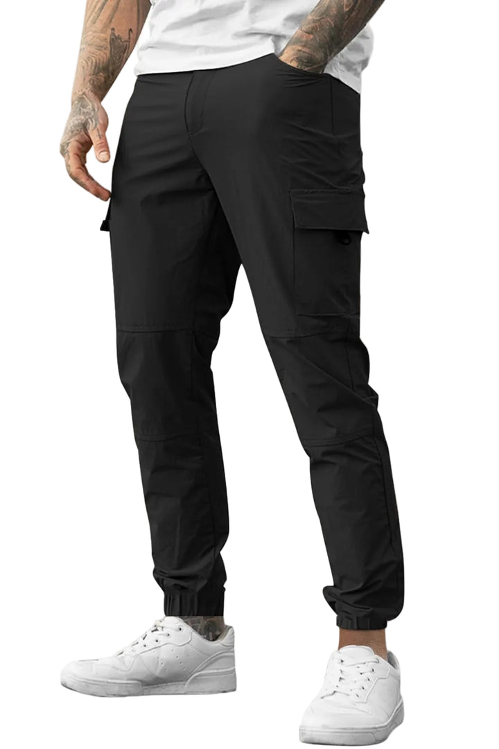 A person wearing black cargo jogger pants with side flap pockets, shown from the waist down against a clean white background. The model is also wearing a white t-shirt and white sneakers.