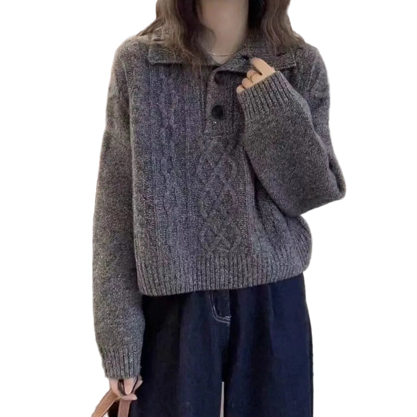 A person wearing a gray cable-knit cropped sweater with a collar and dark buttons, paired with dark blue jeans, standing indoors against a light neutral wall and curtain.