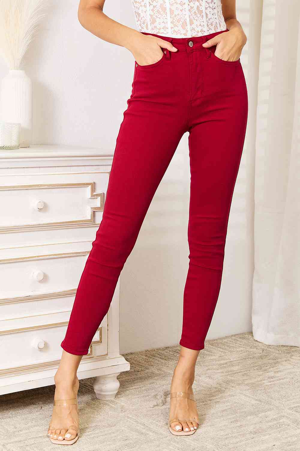 Woman wearing red pants and a white top in a room with a white dresser and curtains.