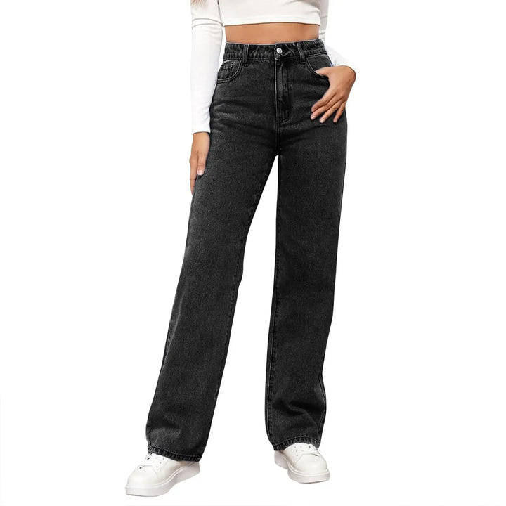 A model wearing a pair of high-waisted, wide-leg black denim jeans with a faded wash, styled with a white long-sleeve crop top and white sneakers against a plain white background.