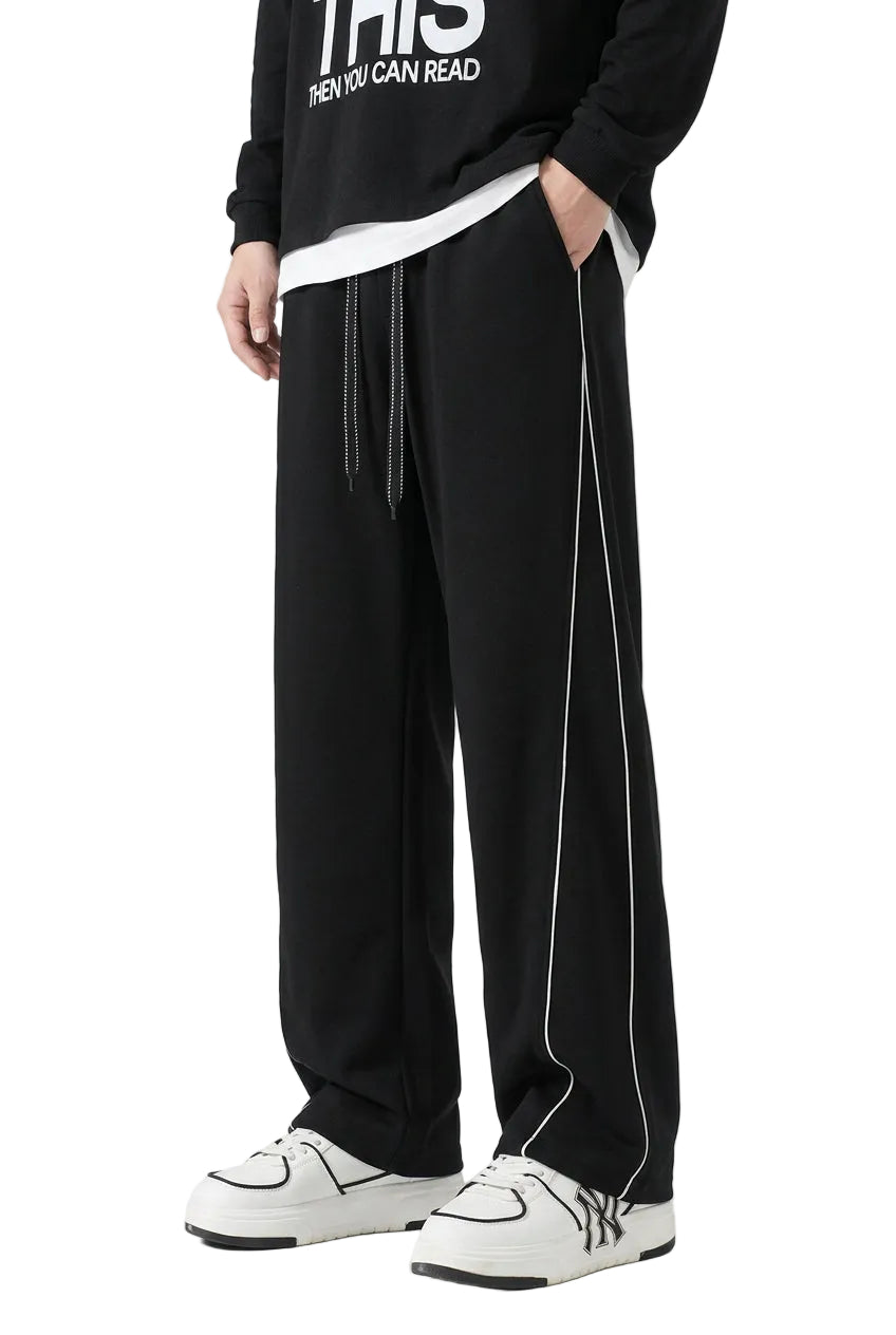 Person wearing black pants with white stripes and a black hoodie on a gray background