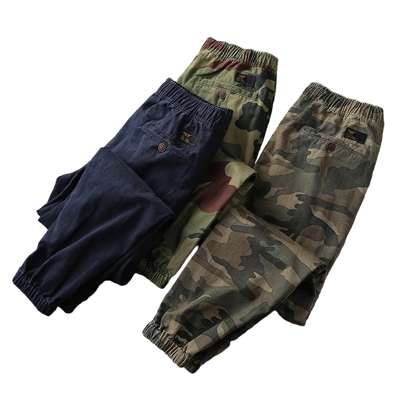 Three pairs of pants in navy, green, and camouflage patterns on a gray surface.