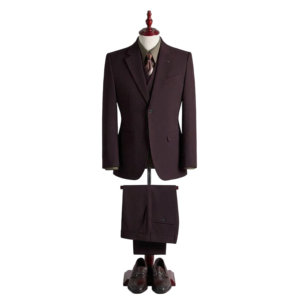 A dark plum-colored three-piece suit displayed on a mannequin, featuring a jacket, vest, trousers, a matching tie, and a pair of dark brown leather loafers, set against a neutral beige background.