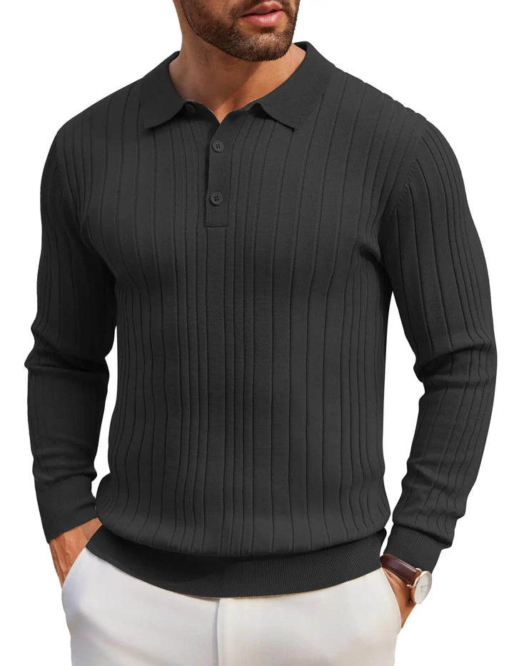 A man wearing a dark charcoal gray ribbed long-sleeve polo shirt with white pants, shown from the chin down against a plain white background.