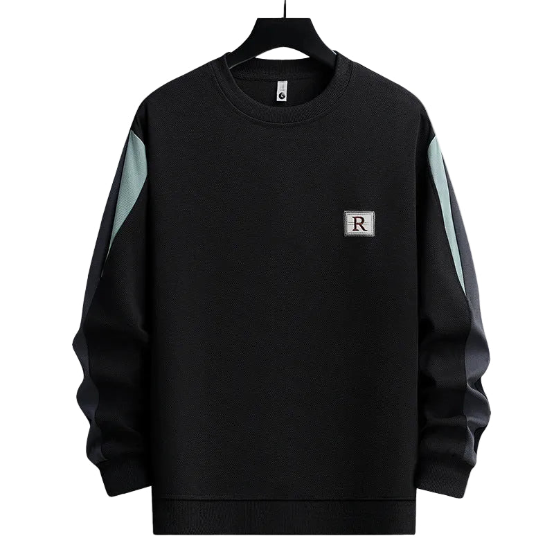 A black crewneck sweatshirt with light blue-green color-blocked panels on the upper sleeves and a small square chest patch featuring the letter 'R', shown on a black hanger against a plain white background.