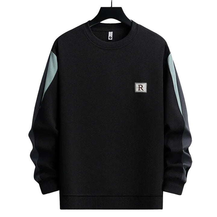 A black crewneck sweatshirt with light blue-green color-blocked panels on the upper sleeves and a small square chest patch featuring the letter 'R', shown on a black hanger against a plain white background.