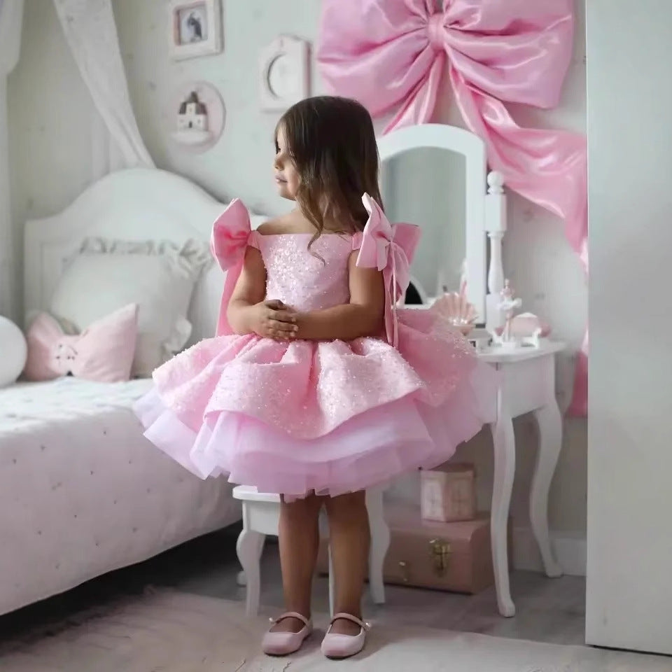 Young girl in a pink dress standing in a bedroom with decorative elements.