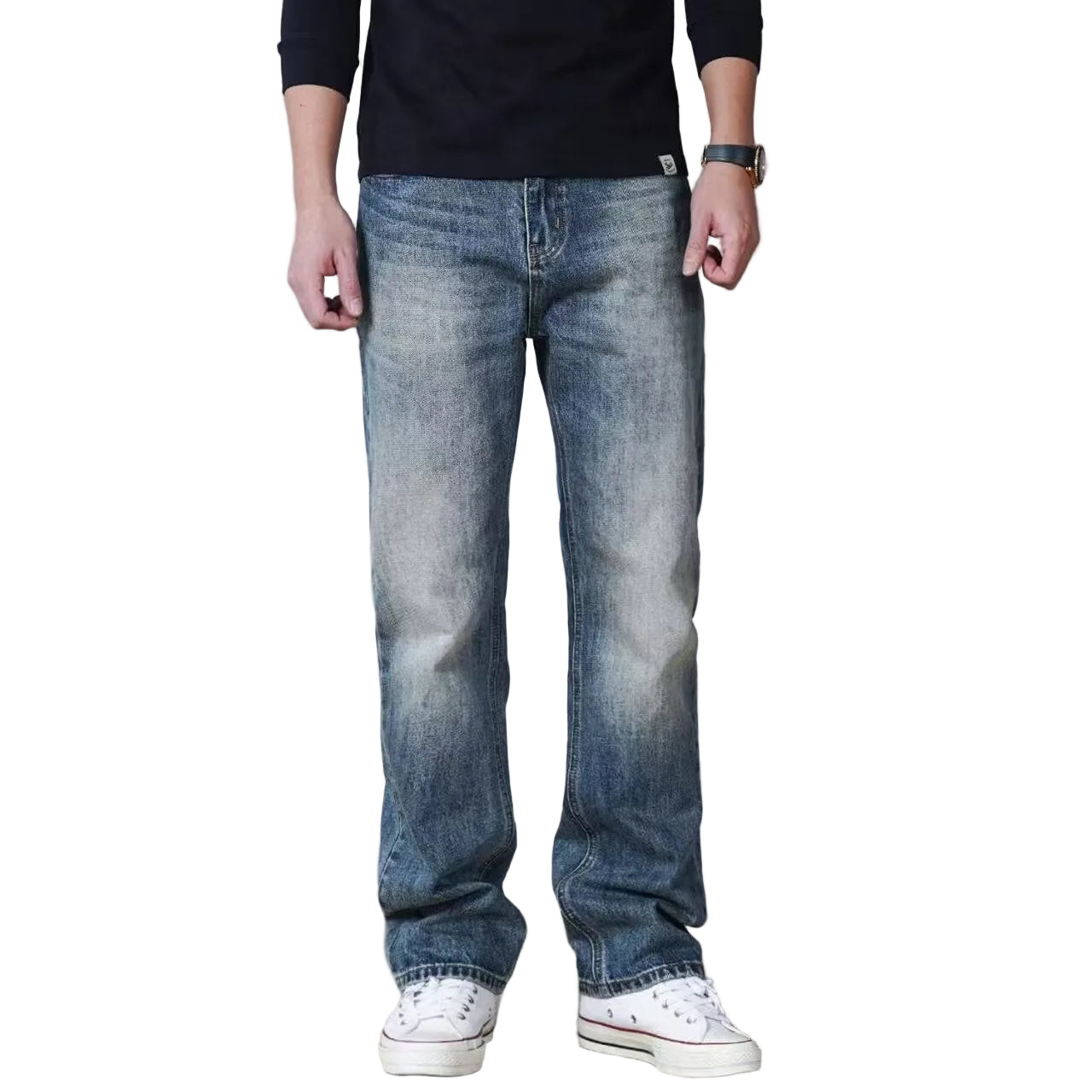 A person wearing light-wash blue denim jeans with a faded wash, paired with a black long-sleeve shirt and white low-top sneakers, standing against a plain gray wall.