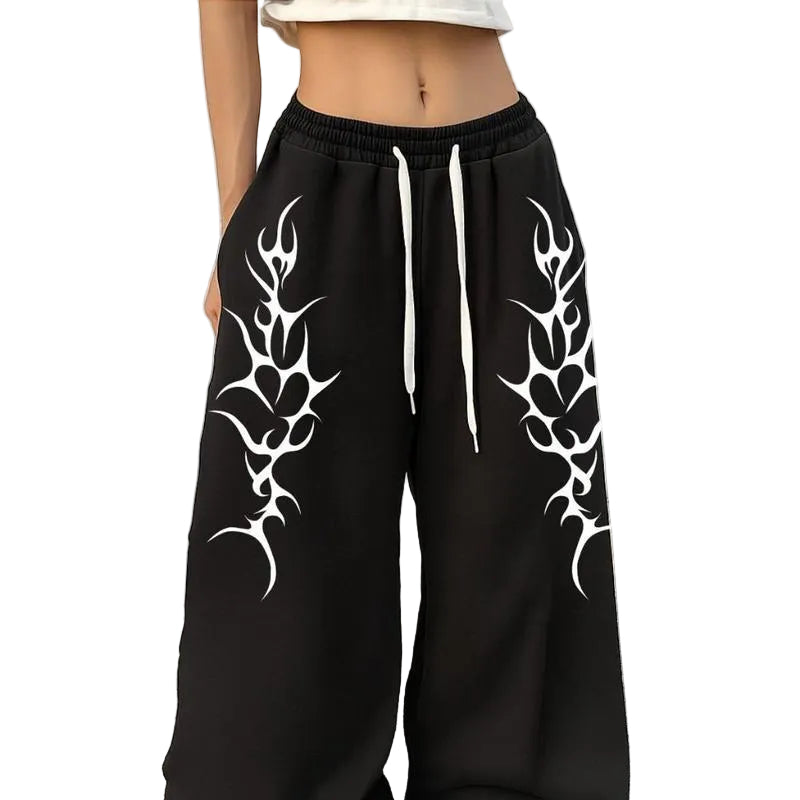 Black wide-leg sweatpants with white tribal-style graphic prints on both legs and white drawstrings, shown on a model standing against a white brick wall.