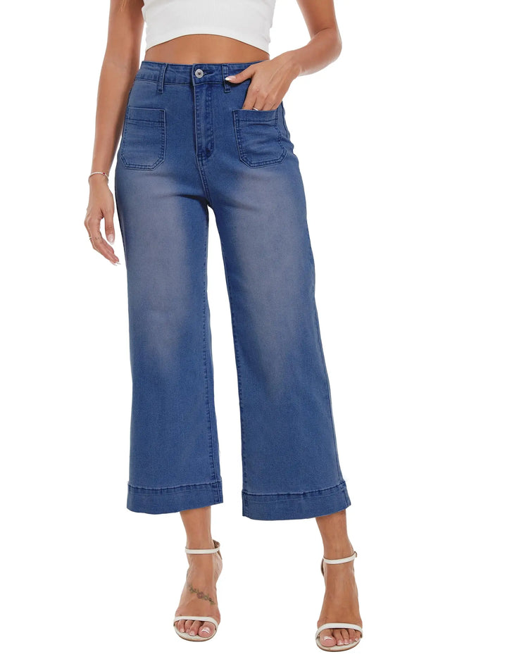 A model wearing blue cropped wide-leg denim jeans with a faded wash, paired with a white crop top and white heeled sandals, shown against a plain white background.